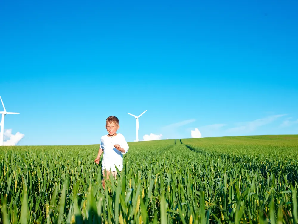 Junge läuft vor Windrädern über ein Feld – Gesundheit und Wohlergehen durch Bewegung