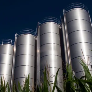 Silberne Silos, die über einem üppigen Maisfeld unter einem klaren blauen Himmel ragen. Biomethan Einspeisung ins Erdgasnetz